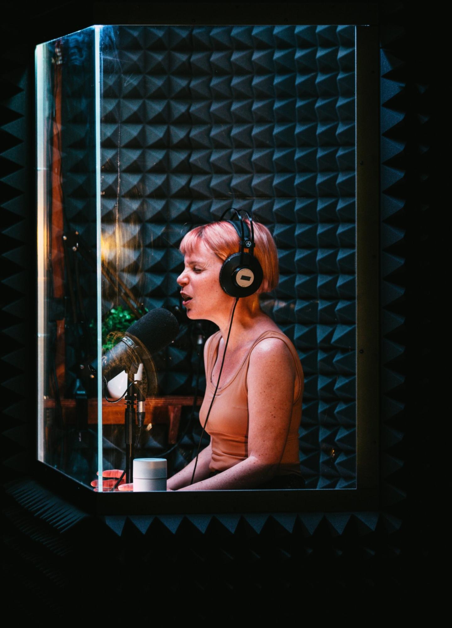 a short haired female sitting in a sound booth talking into a microphone